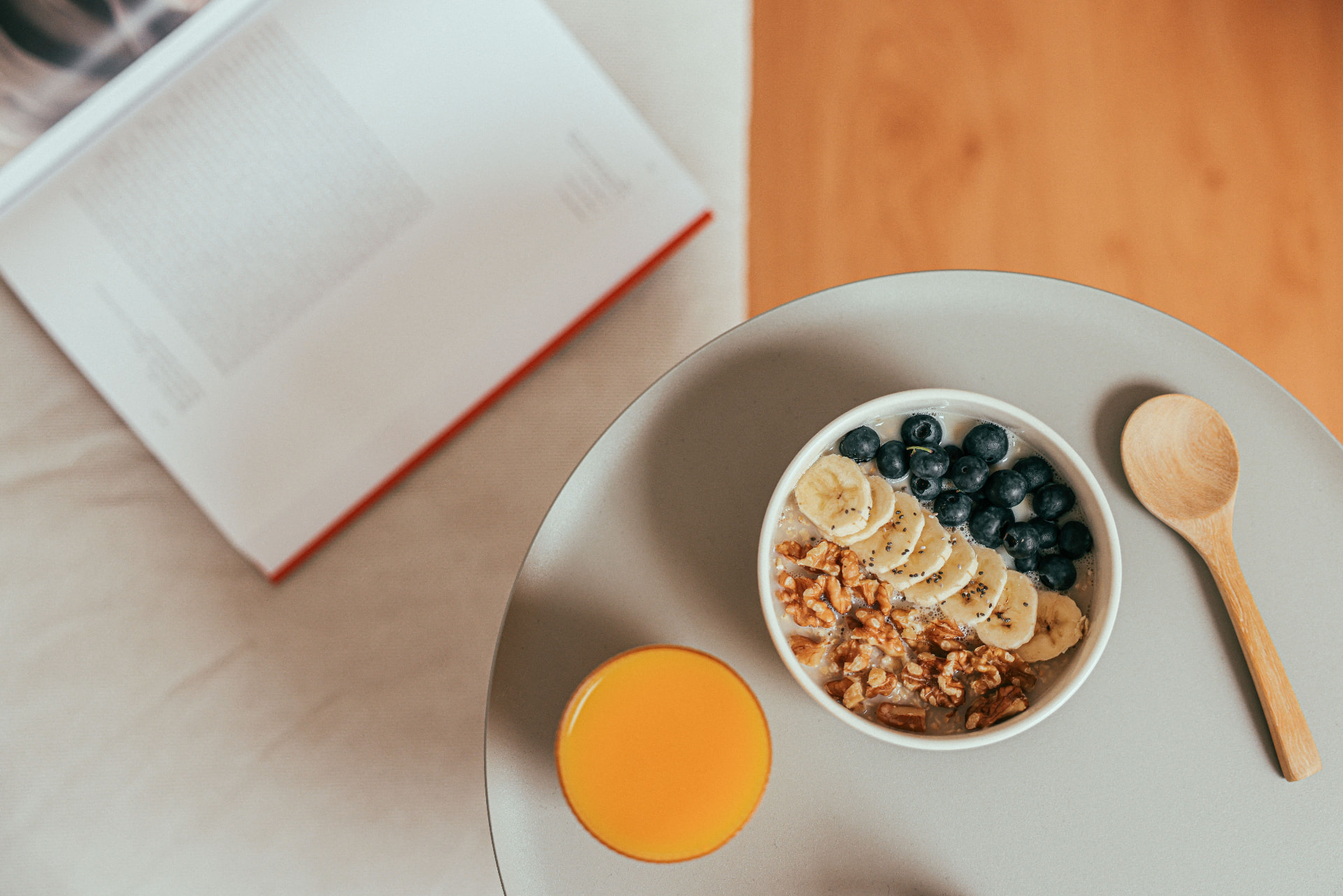 Frukostbord med skål toppad med blåbär, banan, granola och valnötter, samt apelsinjuice och en bok